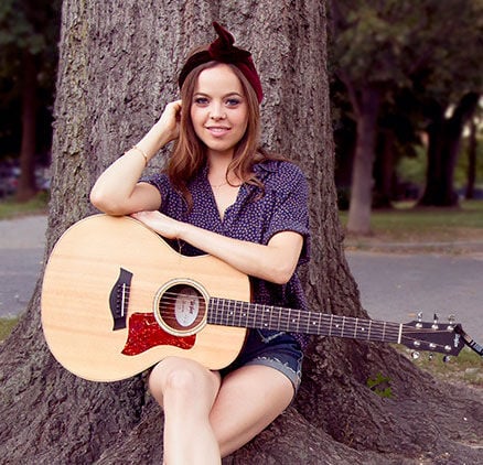 Imagen de Tamara Laurel con su guitarra sentada bajo un árbol