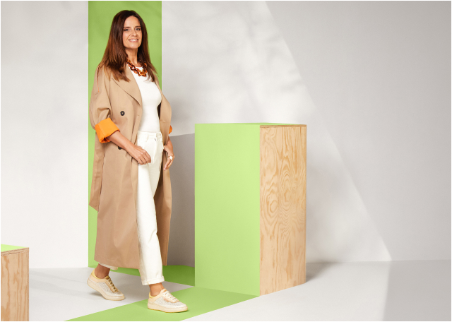 Standing woman in a brown trench coat and white pants, posing with the Pikolinos Mesina
                            style.
