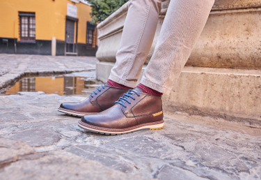 Imagen de pies con botas Pikolinos para hombre. Se trata del modelo Berna, un par de botines en color marrón con cordones en azul y toda la comodidad de dnuestra marca.