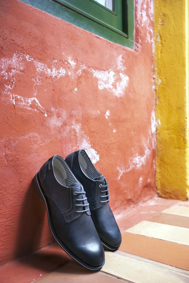 Fotografía de unos zapatos de hombre de Pikolinos en apoyados en una pared roja