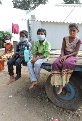 Text on an image of some children with masks on the back of a truck.