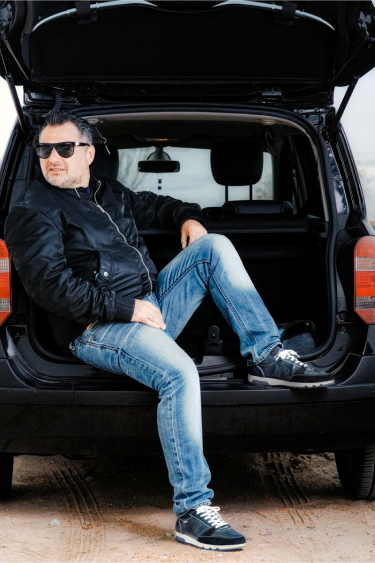 Photograph of Alberto sitting in the trunk of a car with a pair of Pikolinos sports cars.