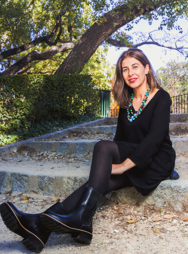Bild von Nuria Pérez, die auf einer Stufe im Park sitzt, schwarz gekleidet und mit Pikolinos-Stiefeln.
