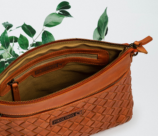Cropped image of an open women's bag, the inner lining and some green leaves on a white background.