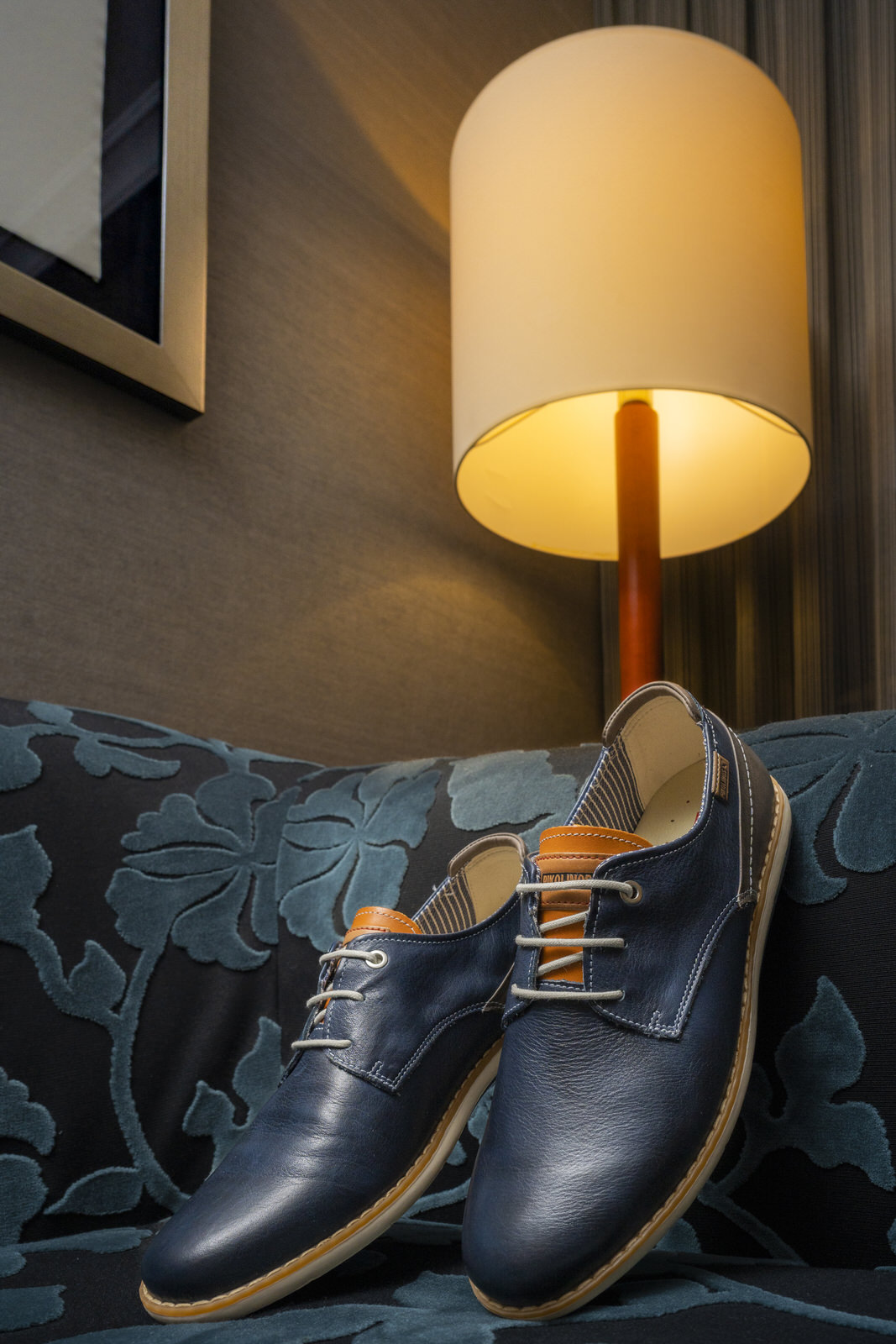 Imagen de un par de zapatos de hombre Pikolinos sobre un sofá, con una lámpara detrás