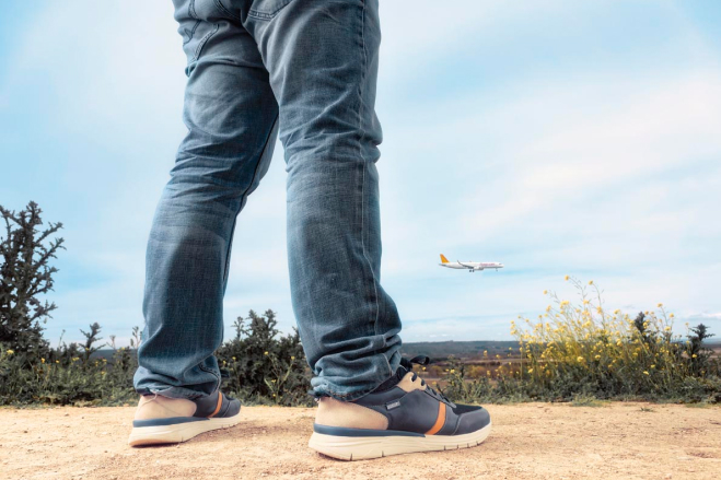 Bild von Albertos Beinen mit Pikolinos-Turnschuhen und einem Flugzeug am Himmel im Hintergrund.