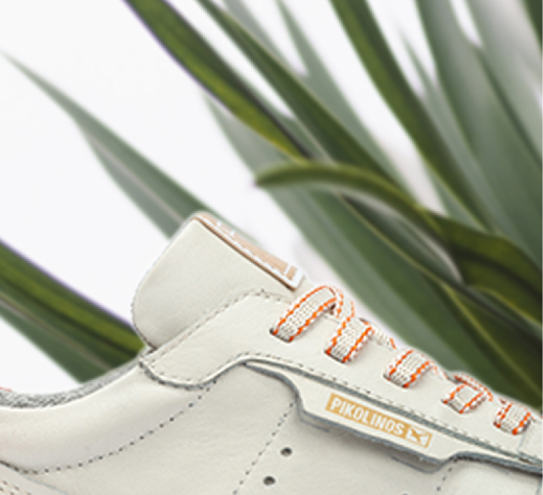 Cropped image of white shoes, with a background with green leaves.