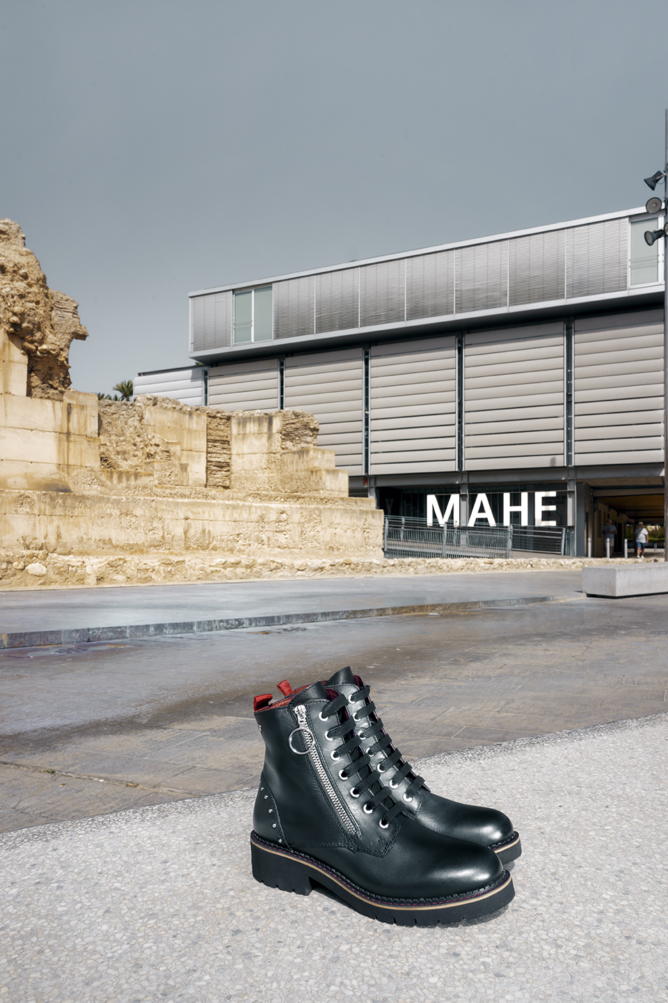 Abbildung eines Paars Pikolinos-Stiefel in Schwarz für Damen und im Hintergrund das archäologische und historische Museum von Elche.