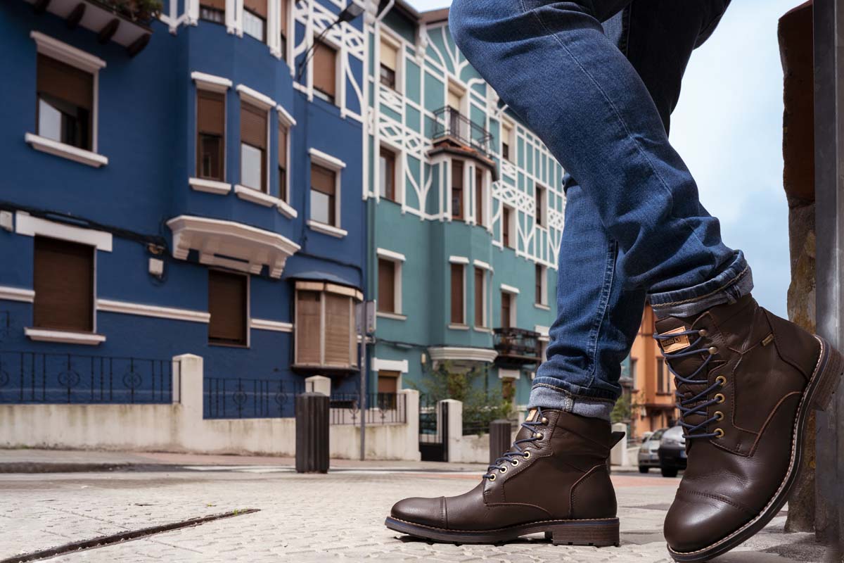 Fotografía de un botín de hombre con las casas de colores de fondo