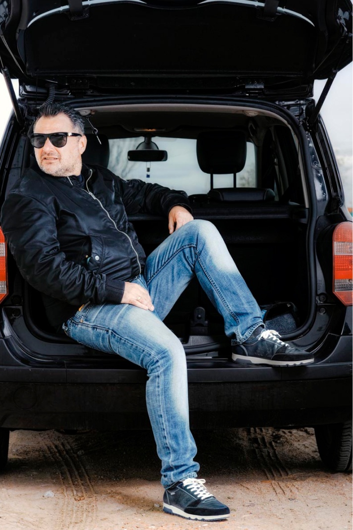Photograph of Alberto sitting in the trunk of a car with a pair of Pikolinos sports cars.