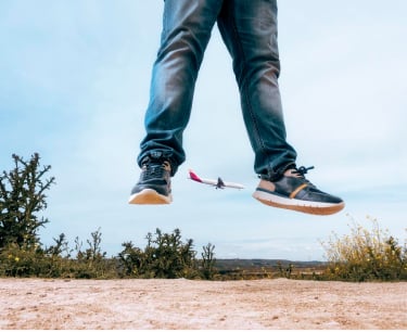 Photograph of Alberto's legs in the air jumping with some Pikolinos sneakers and a plane in the background.