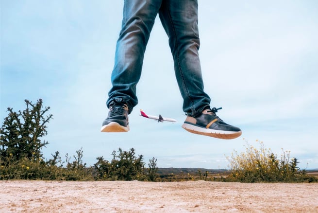 Foto von Albertos Beinen in der Luft, die mit einigen Pikolinos-Turnschuhen und einem Flugzeug im Hintergrund springen.