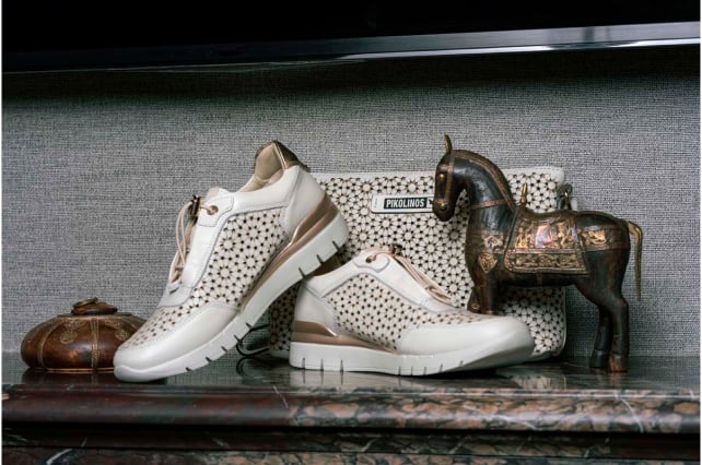 Photograph of Pikolinos women's sneakers on a street in Alicante with a stone coat of arms in the background on the wall