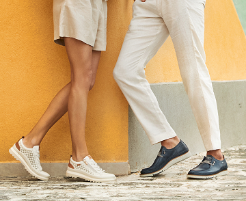 Image of feet wearing Pikolinos. A woman and a man, facing each other, in front of
                    a wall.