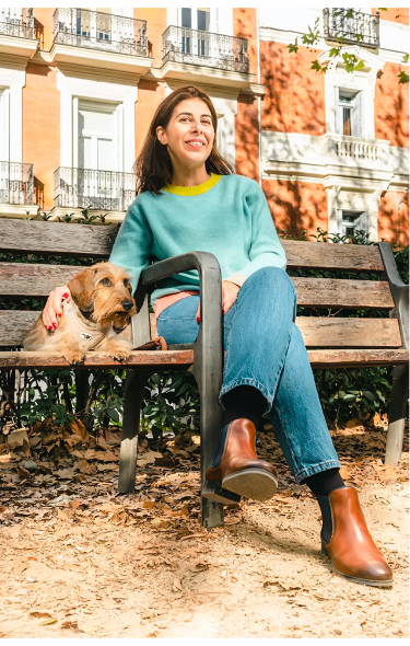 Image de Nuria Pérez assise sur un banc avec son chien et portant des bottines Pikolinos.