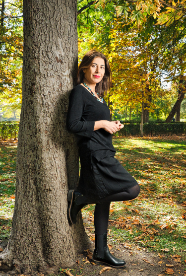 Image de Nuria Pérez appuyée contre un arbre dans le parc, vêtue de noir et avec des bottes Pikolinos.