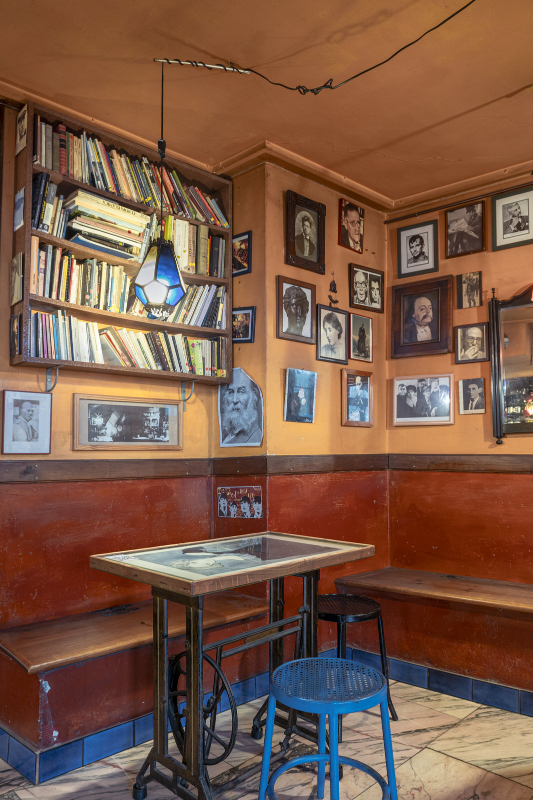 Imagen del interior de la cafetería, en la pared hay cuadros, libros y una mesa con taburetes