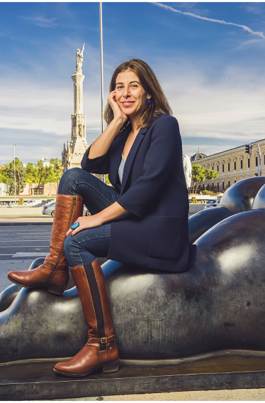 Bild von Nuria Pérez, die auf einer Statue sitzt, mit Madrid im Hintergrund. Er trägt Pikolinos-Stiefel.