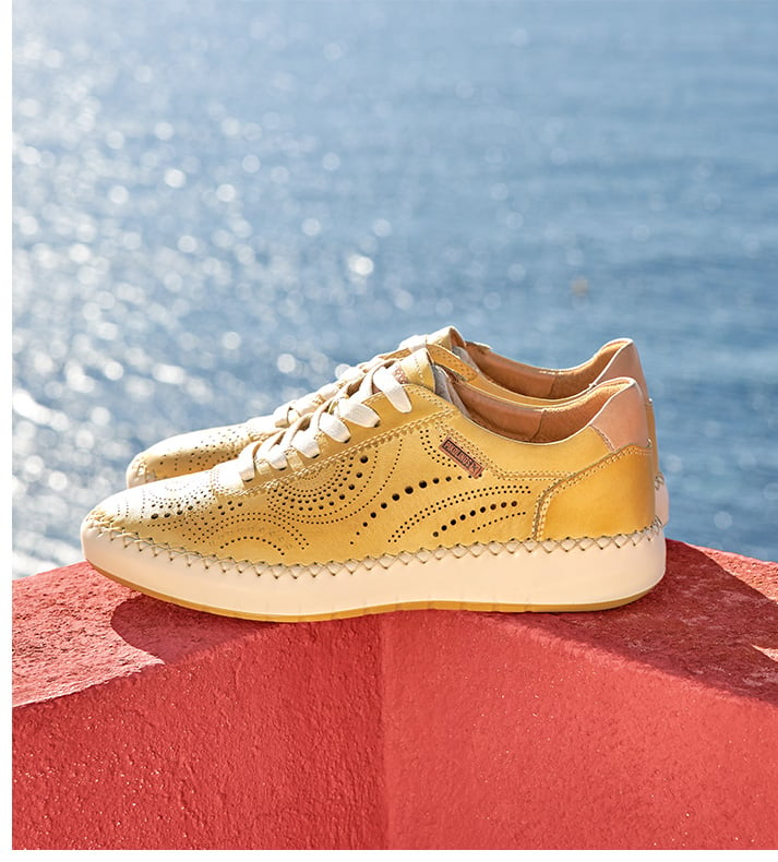 Die-cut leather sneaker for women in yellow and thick white sole on a wall and with the sea in the background